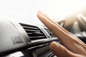 Close-up of a hand checking car A/C airflow from a dashboard vent on a bright day. For reliable car A/C repair and comprehensive auto repair in Englewood, CO, visit Autovisions.