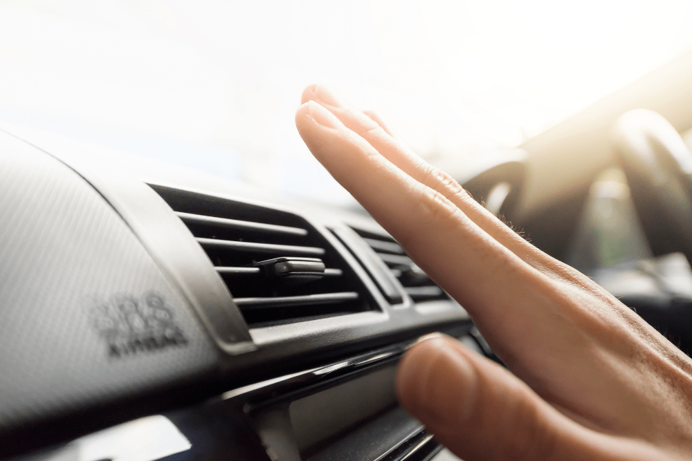 Close-up of a hand checking car A/C airflow from a dashboard vent on a bright day. For reliable car A/C repair and comprehensive auto repair in Englewood, CO, visit Autovisions.