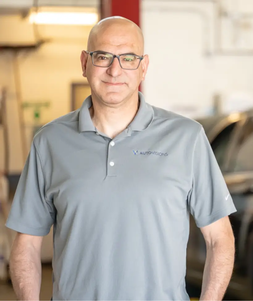 Image of Autovision's owner Nathan Bryant in a gray polo shirt standing confidently in his auto repair shop in Englewood, CO