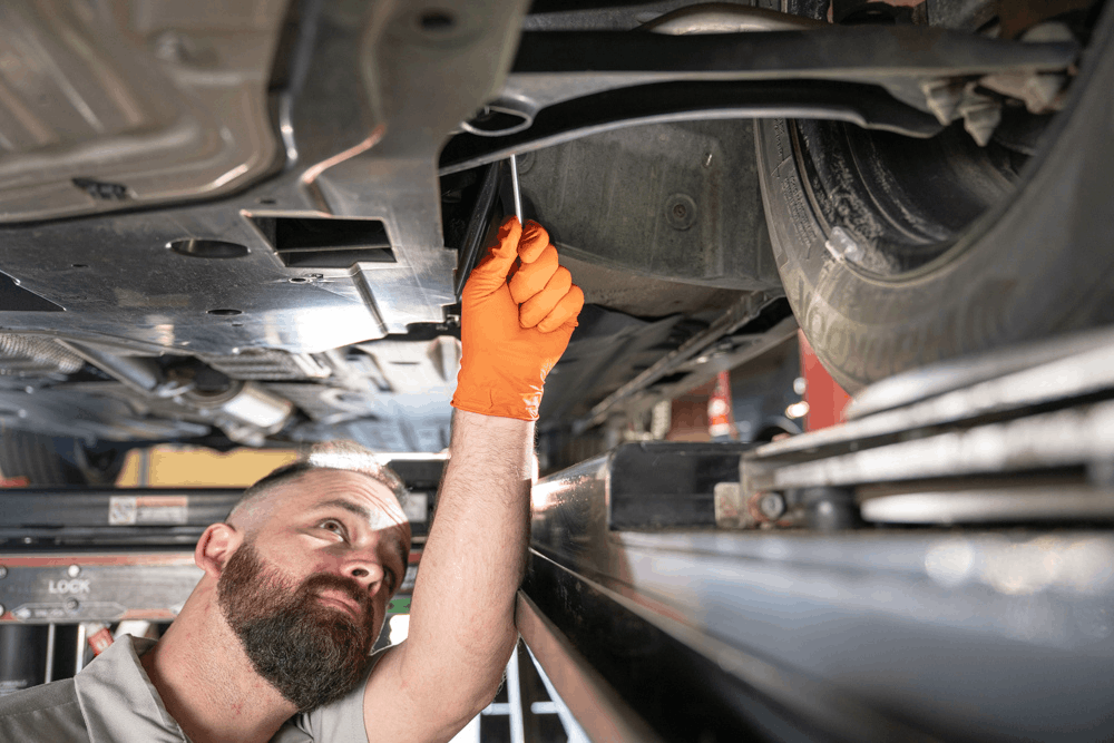 Auto repair in Englewood, CO, at Autovisions. Auto technician inspecting the underside of a vehicle during a comprehensive suspension and undercarriage inspection at a professional auto repair shop.