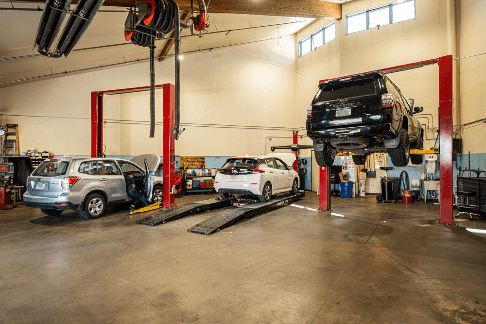 Auto repair near Littleton, CO at Autovisions. Image of multiple vehicles inside the service shop, including an SUV raised on a lift for inspection and maintenance.