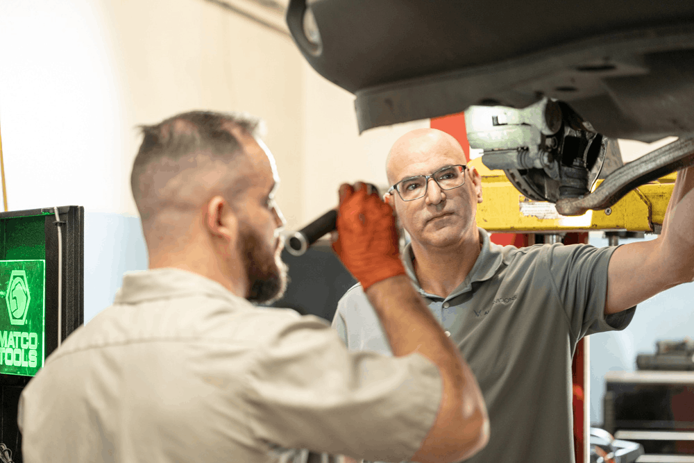 Vehicle inspection, auto repair in Englewood, CO at Autovisions.Image of two technicians examining suspension components beneath a vehicle on a lift to support safe, reliable handling.